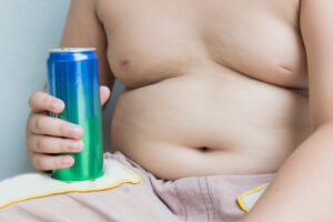 Bambino sovrappeso a torso nudo con lattina di bevanda zuccherata in mano; concept: alimentazione, obesità, bambini, cattive abitudini, sugar tax, fegato grasso