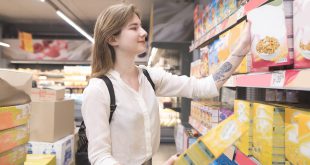 Happy young woman chooses flakes in a supermarket and smiles. A joyful buyer buys products in a supermarket. A girl with packs of quick breakfasts in the hands of the store