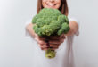 Young woman showing broccoli to camera.