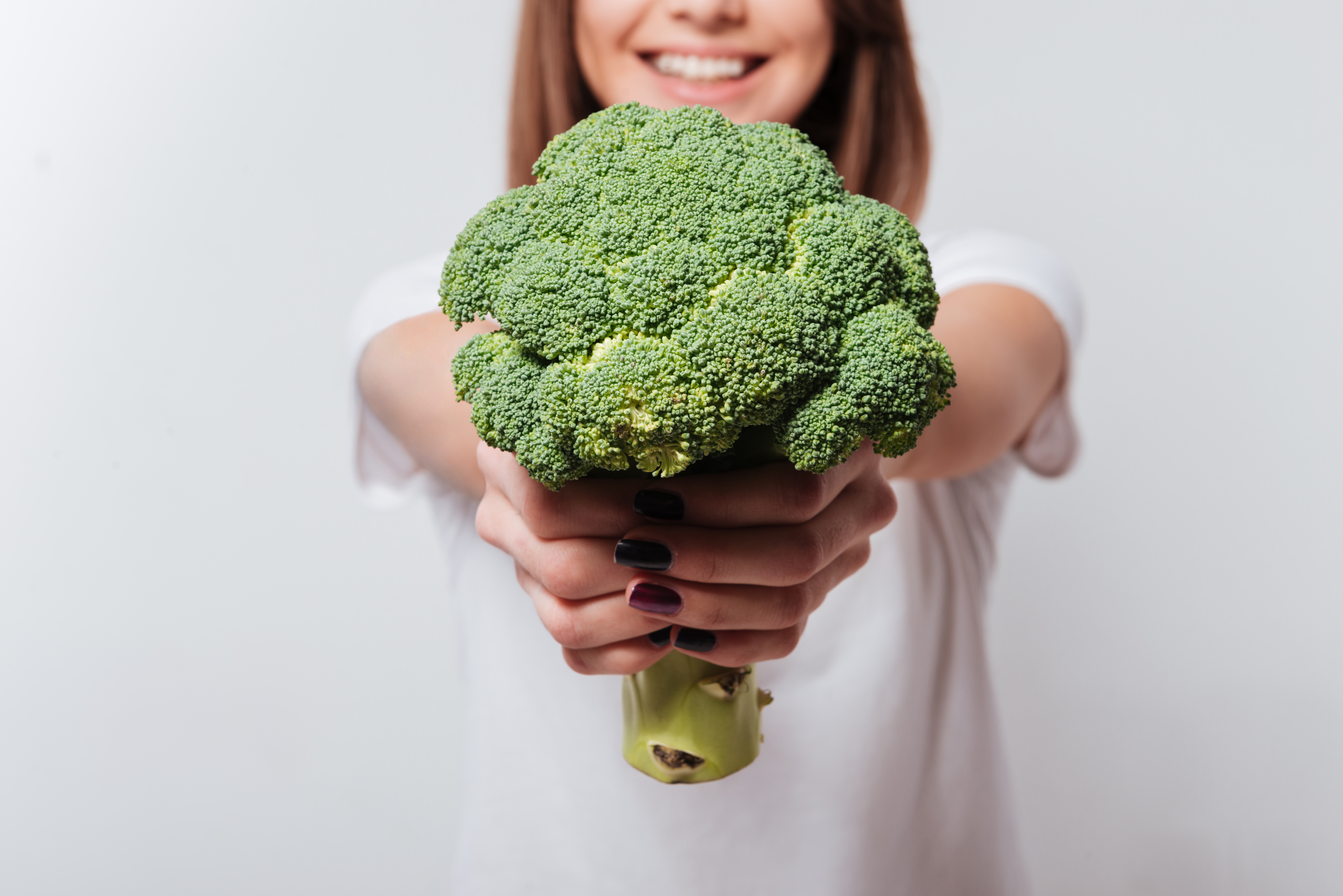 Young woman showing broccoli to camera.