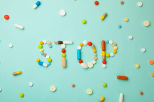 Word STOP from colored pills and capsules on green background. Medicines and tablets kill