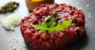 Beef tartare served with an egg yolk on a grey surface, close up