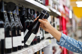 Donna preleva bottiglia di vino rosso dallo scaffale del supermercato, concept: alcol