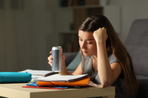 Studente che prepara l'esame memorizzando gli appunti con in mano una bevanda energetica durante la notte a casa energy drink