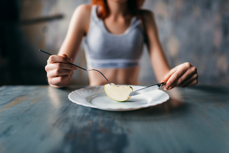 Donna con top sportivo mangia con coltello e forchetta fetta di mela su un piatto: concept: sport, dieta, digiuno, disturbi del comportamento alimentare, dca