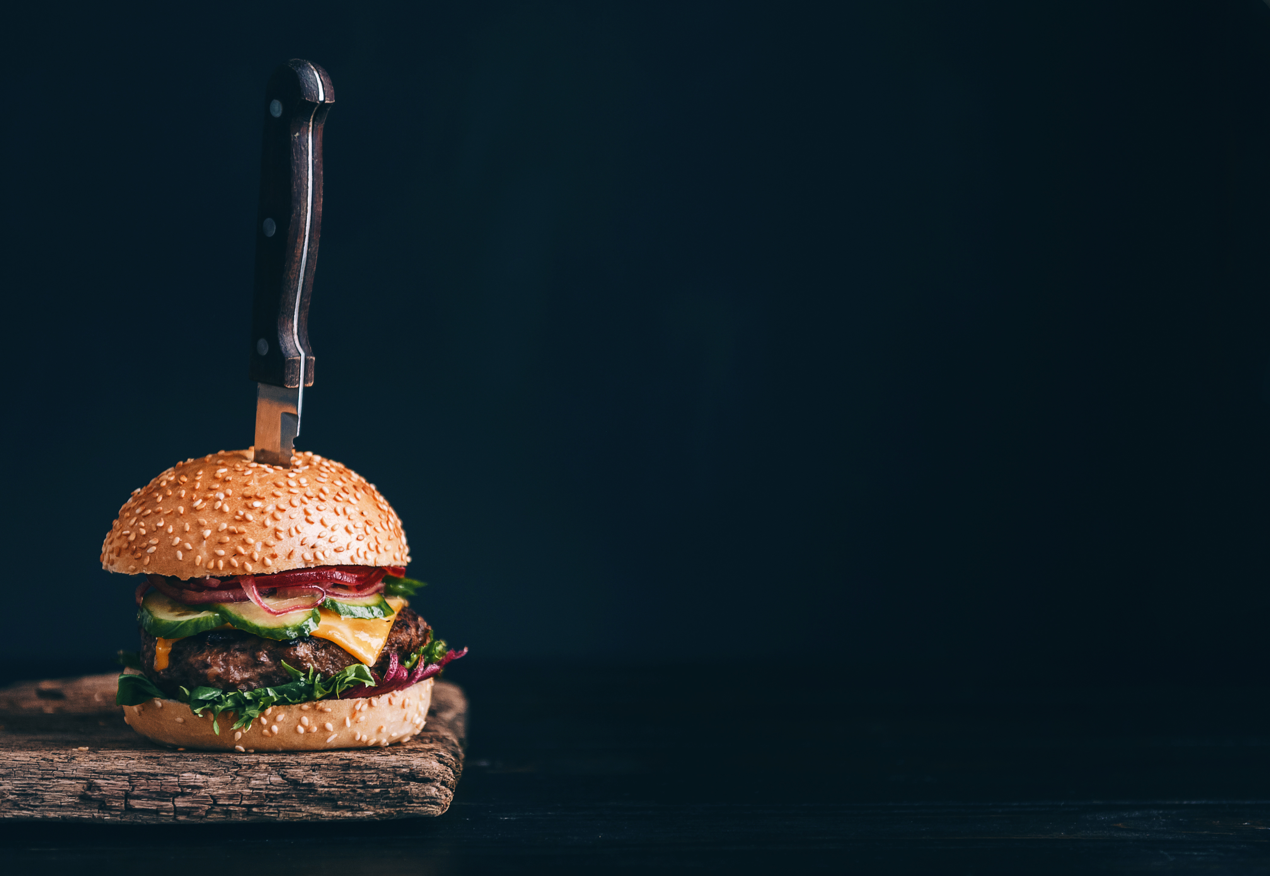 Panino con hamburger infilzato da un coltello su sfondo nero; conpcet: fast food, junk food