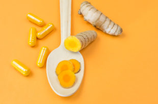 Yellow curcuma root with wooden spoon and pills on orange background