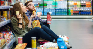 Couple sitting on the supermarket floor and eating snacks junk food