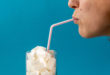 Profile of a young woman drinking with a red stripes straw from a glass filled with sugar cubes on blue background. Junk food, unhealthy diet, too much sugar on drinks, nutrition concept