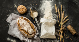 Bread, flour bag, wheat and measuring cup on black