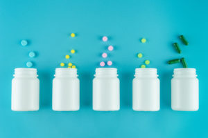 Farmaci, integratori, antibiotici o probiotici in pillole, compresse o capsule rovesciate da bottigliette in fila su sfondo azzurro
