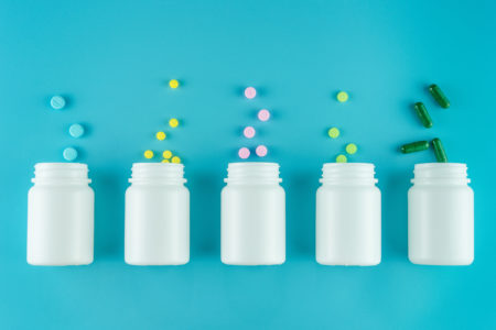 Farmaci, integratori, antibiotici o probiotici in pillole, compresse o capsule rovesciate da bottigliette in fila su sfondo azzurro