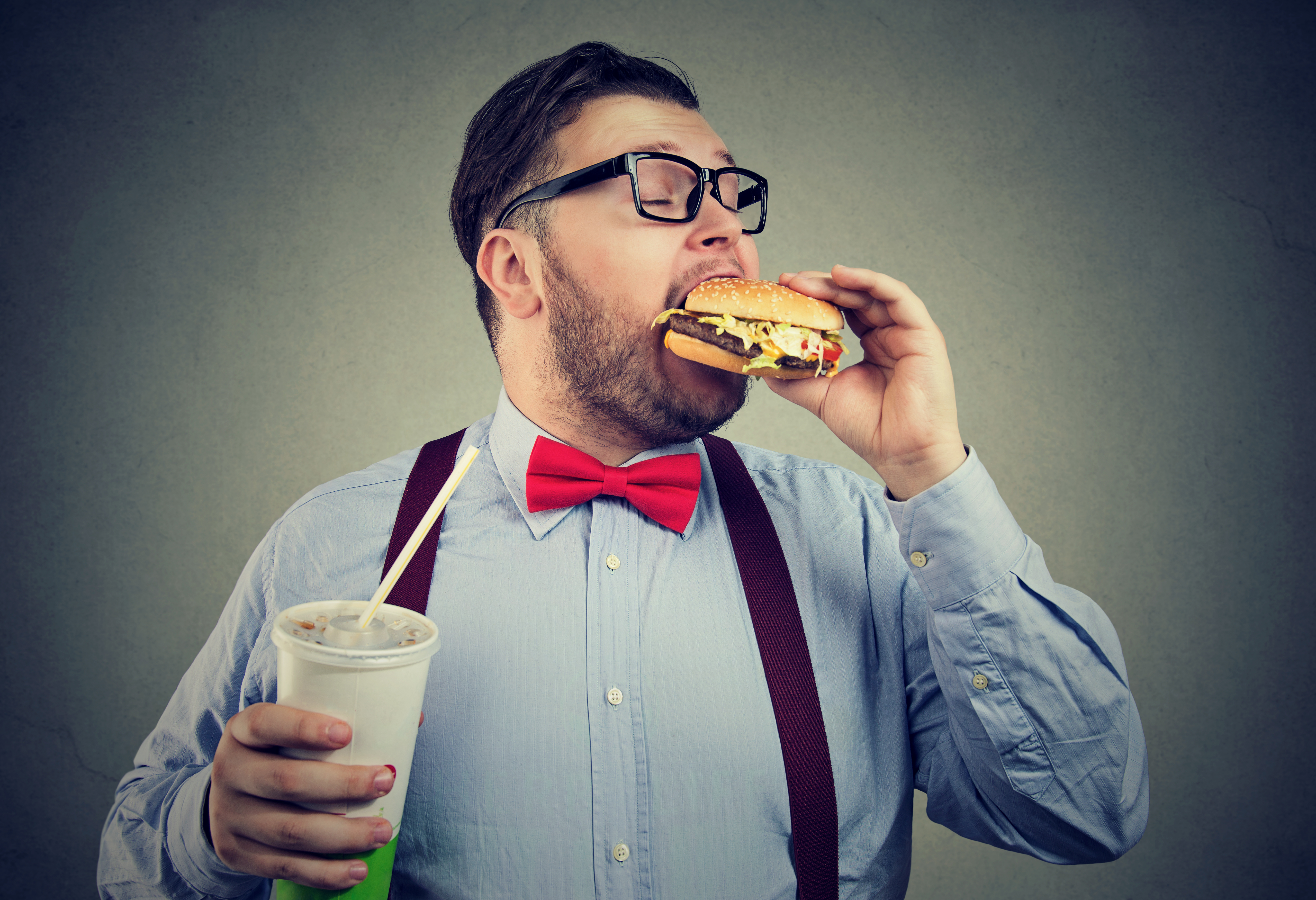 Uomo in sovrappeso mangia cibo spazzatura: hamburger e bibita zuccherate