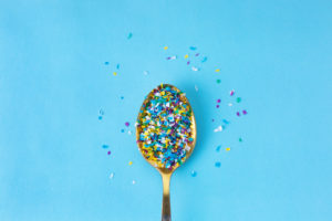 Microplastiche colorate su un cucchiaino dorato su sfondo azzurro