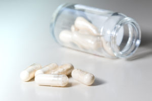Capsule di integratori alimentari o farmaci contenenti polvere bianca; sullo sfondo bottiglietta in vetro con altre capsule; concept: integratore, farmaci, antibiotici, probiotici