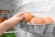 Woman taking chicken egg from refrigerator door shelf, closeup