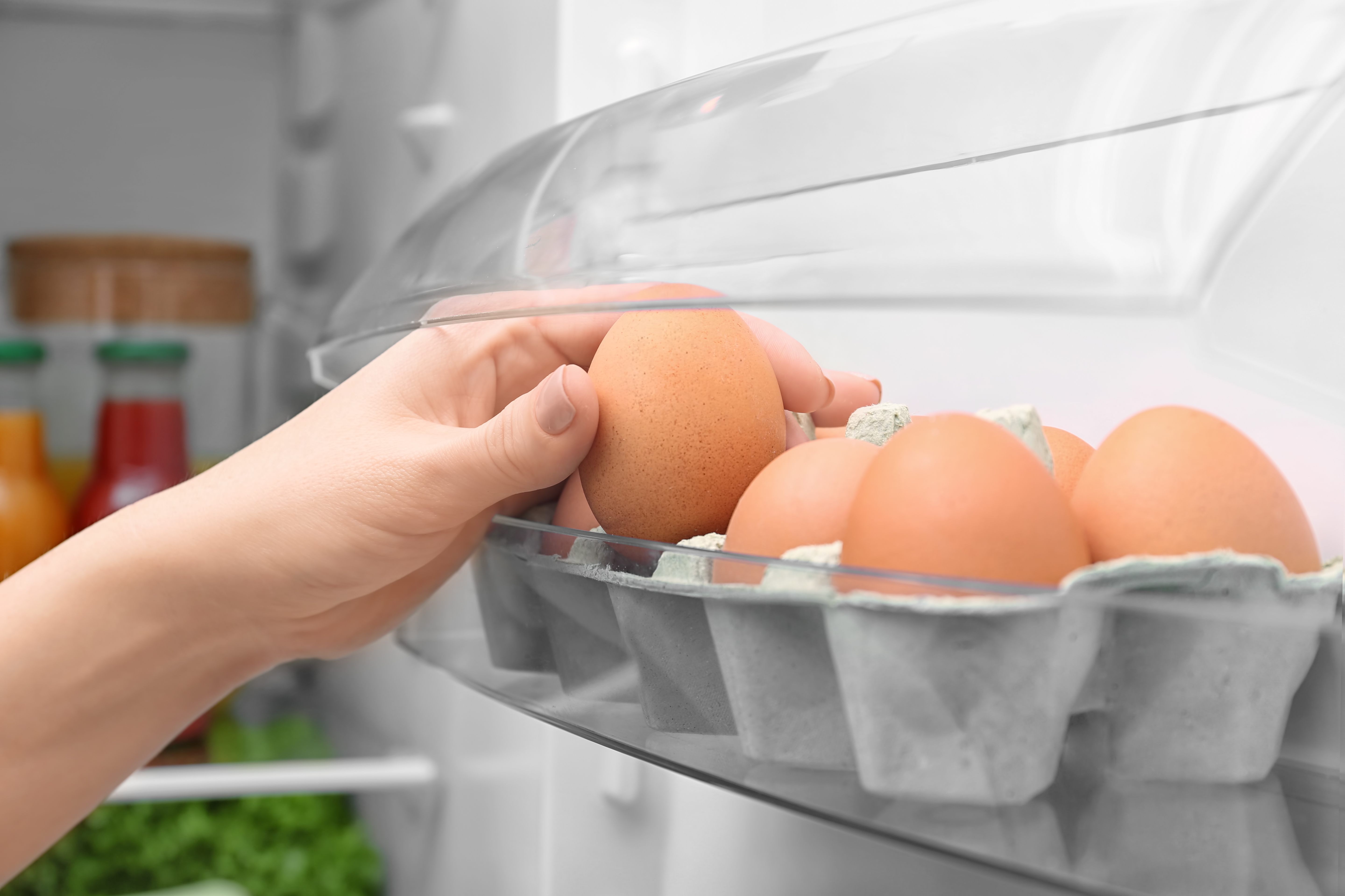 Donna prende un uova da un cartone nella porta del frigorifero; concept: uova, conservazione