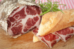 Pezzo di coppa tagliato su un tagliere accanto a panino con coppa a fette; concept: salumi