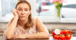 Mature blond-haired woman sitting at the table having food allergy