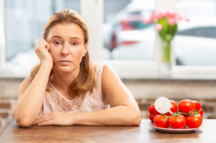 Mature blond-haired woman sitting at the table having food allergy