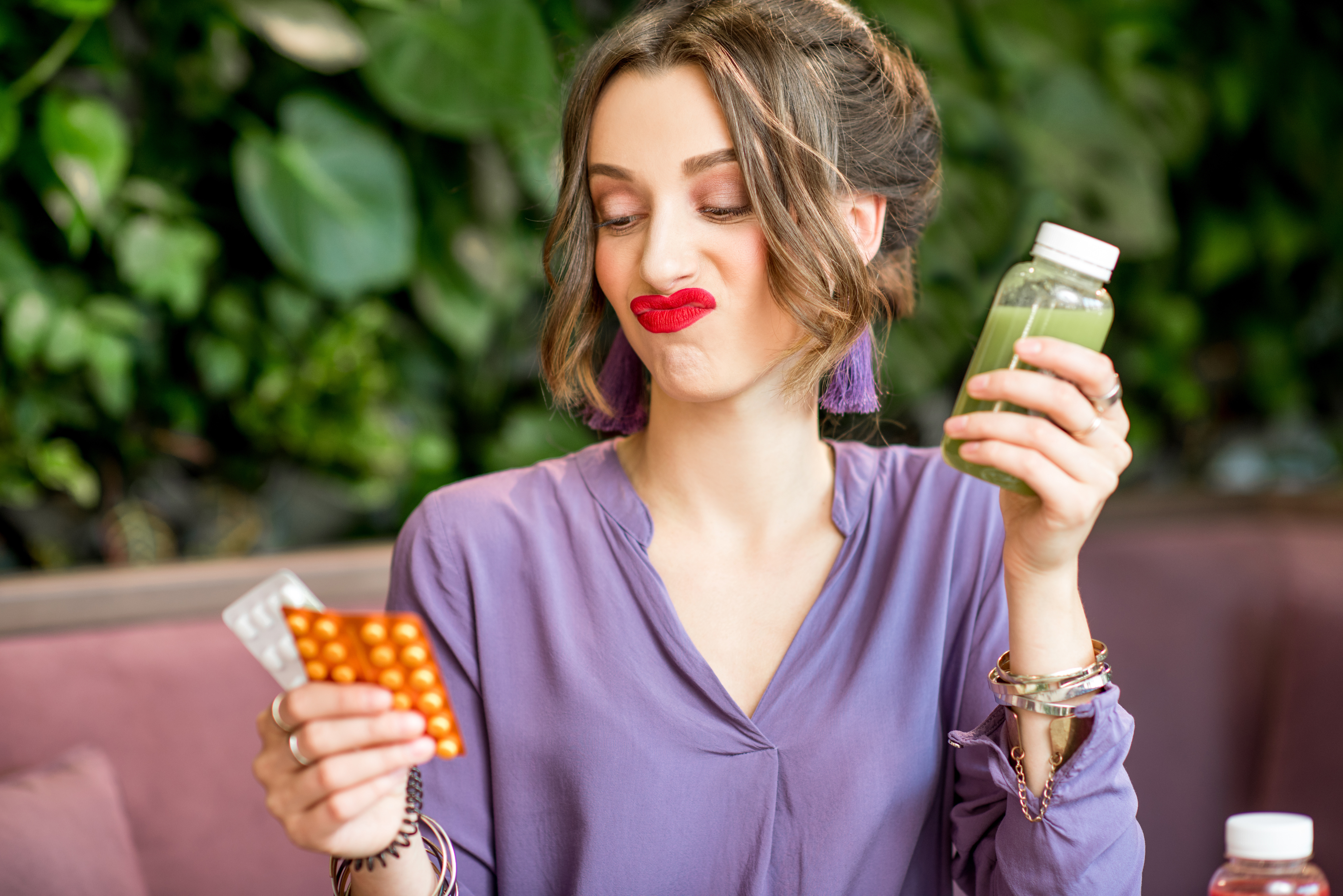 Woman looks undecided at blister packs of pills, while holding a smoothie with her other hand