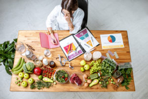 Dietista, dietologa o biologa nutrizionista elabora dieta su una scrivania piena di alimenti