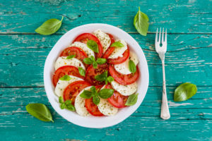 Deliziosa insalata caprese con pomodori maturi e mozzarella con foglie di basilico fresco. Cibo italiano.