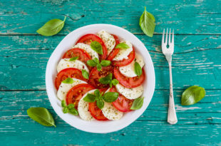 Delicious caprese salad with ripe tomatoes and mozzarella cheese with fresh basil leaves. Italian food.