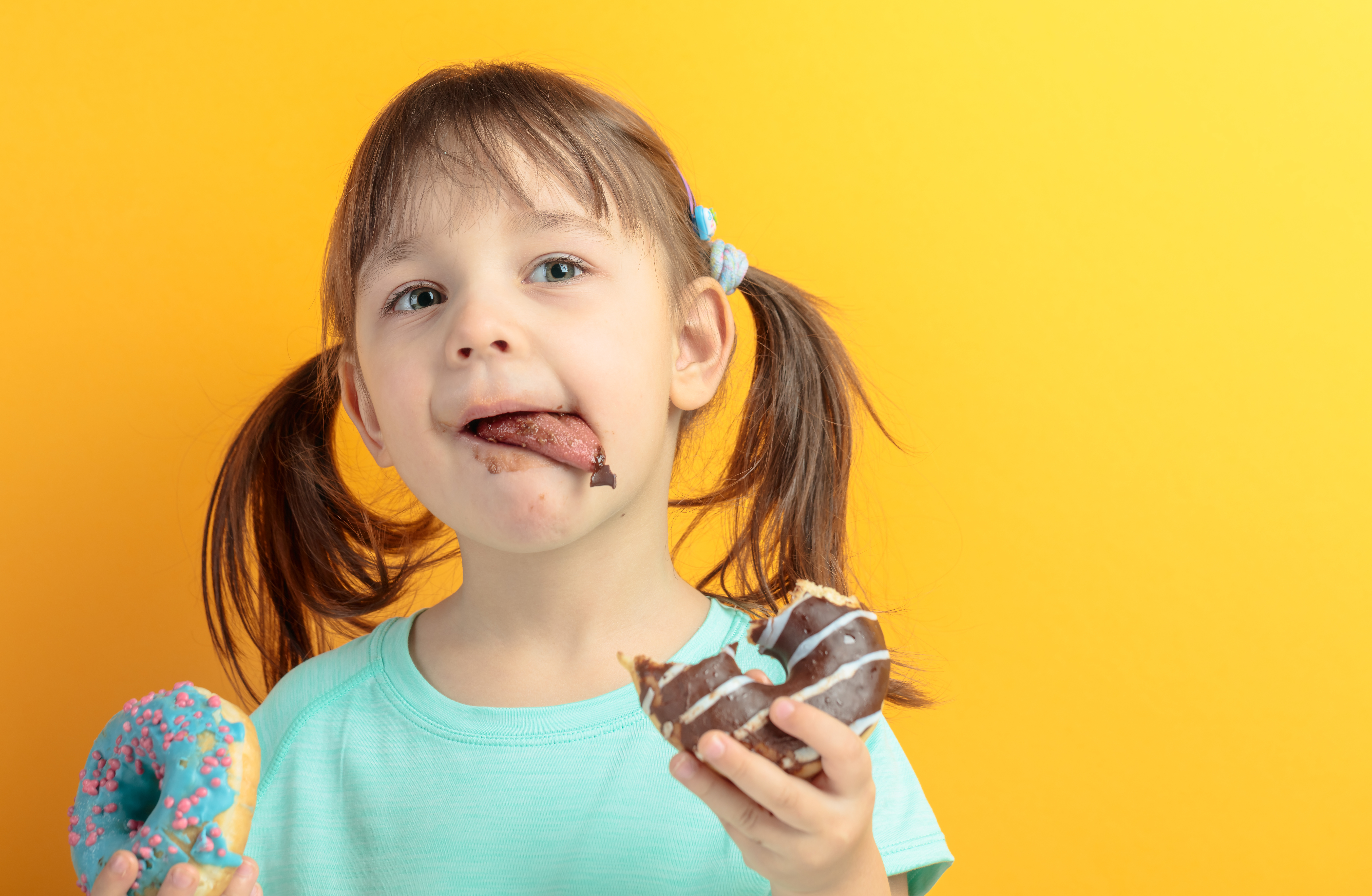 bambina che mangia ciambelle si lecca le labbra sporche di cioccolato
