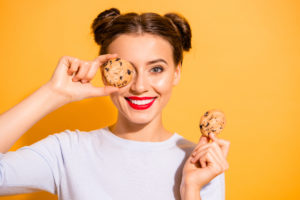 Close up photo of charming lovely hipster playing with cakes pies candies in kitchen preparing for birthday dressed in white woolen pullover isolated over colorful background