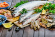 Prodotti ittici assortiti su un tagliere di legno: branzini, orate, gamberi, calamari, cozze, ostriche