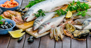 Prodotti ittici assortiti su un tagliere di legno: branzini, orate, gamberi, calamari, cozze, ostriche