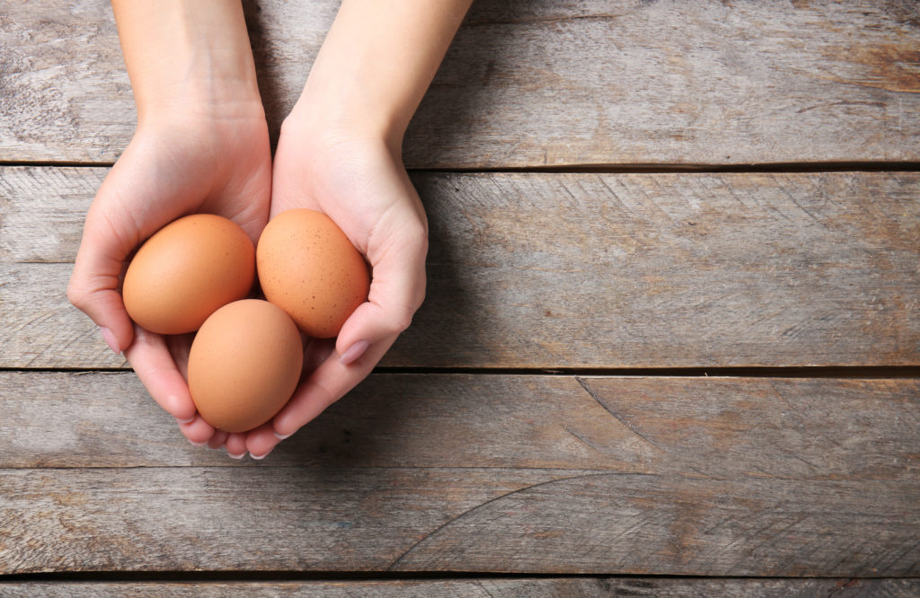 Woman holding raw eggs on wooden background