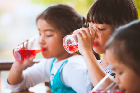 roup of asian children drinking red juice water with ice from glass together in the summer time