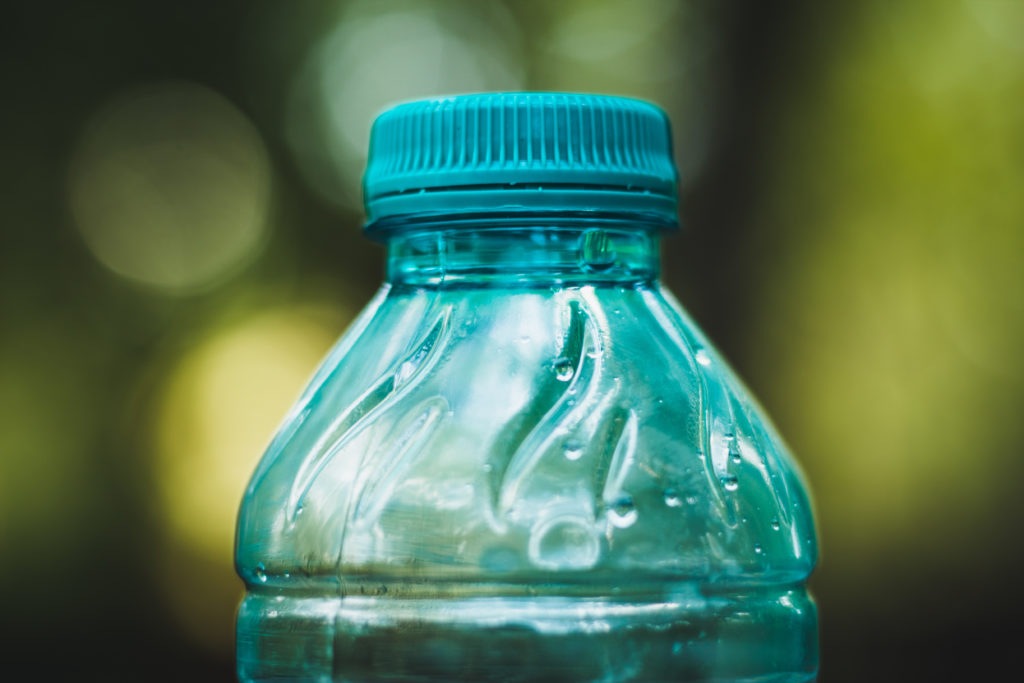 Closeup of a transparent plastic bottle with blue cap with a green background – Empty recyclable beverage container – Concept image for a clean environment and recycling