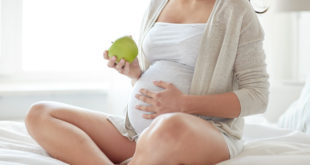 close up of pregnant woman eating apple at home