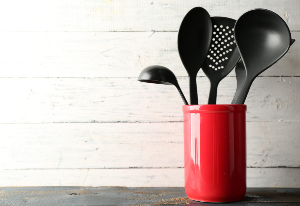 Plastic kitchen utensils in red cup on wooden background