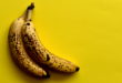 Two ripe bananas with brown spots on the bright yellow table, top view, empty space.