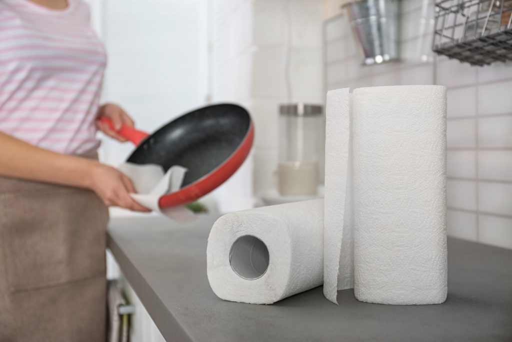 Woman wiping frying pan in kitchen, focus on paper towels