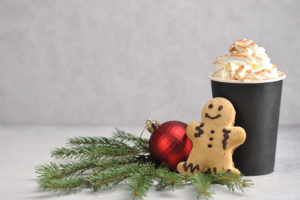 Cappuccino and cinnamon in a paper cup. Coffee is complemented by a gingerbread man and Christmas tree decoration.