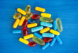 Capsule e capsule molli gialle, rosse e azzurre su uno sfondo blu; concept di farmaci e integratori