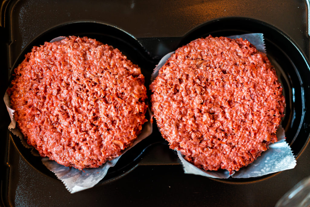 Flat top closeup of two raw uncooked red vegan plant based meat burger patties in packaging