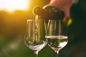 Due calici di vino bianco con bottiglia in atto di versare e il sole sullo sfondo