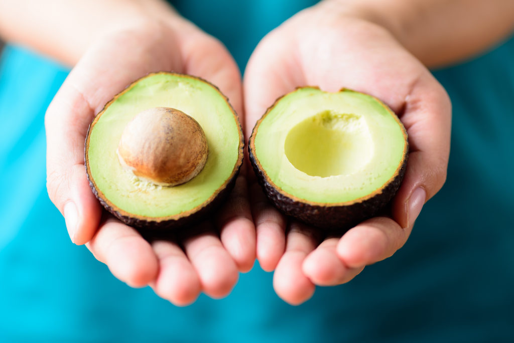 Mani femminili tengono le due metà di un avocado; concept: frutta esotica