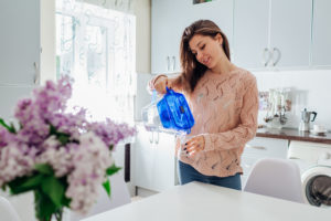Woman pouring filtered water from filter jug into glass on kitchen. Modern kitchen design. Healthy lifestyle