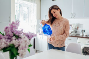 Woman pouring filtered water from filter jug into glass on kitchen. Modern kitchen design. Healthy lifestyle