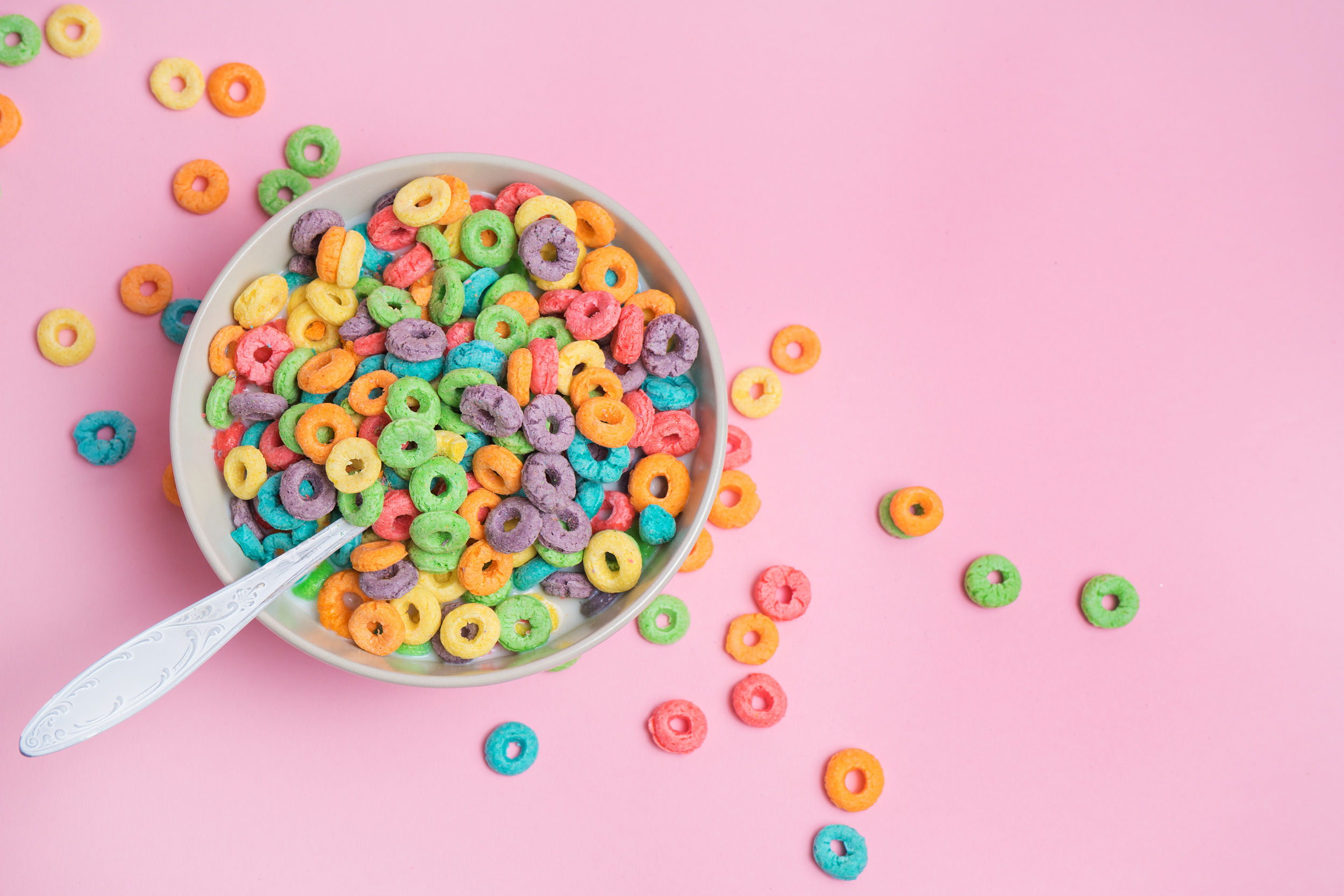 Cereali da colazione colorati in una tazza con cucchiaio, appoggiata su una superficie rosa