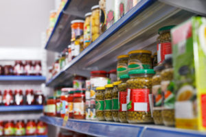 Dettaglio di conserve di verdure in vasetto di vetro sugli scaffali di un supermercato; etichette