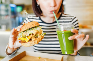 Ragazzo beve uno smoothie verde mentre tiene in mano un panino con burger vegetale