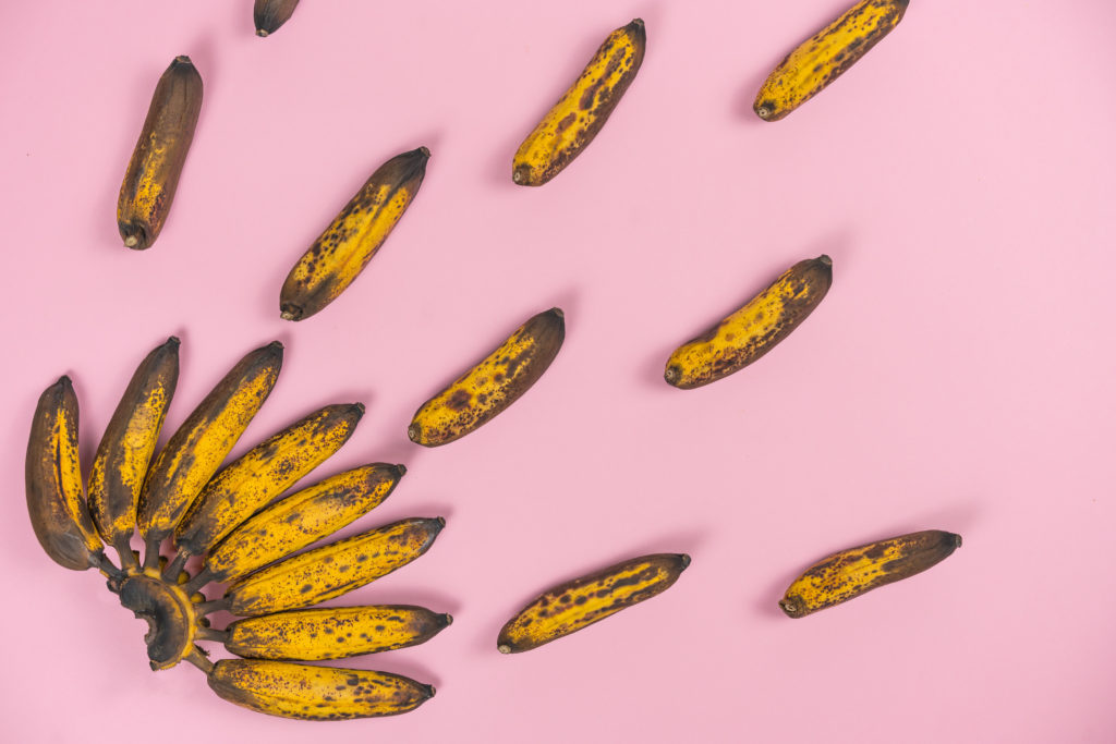 mazzo di mini- banane rovinate e troppo mature su uno sfondo rosa pallido